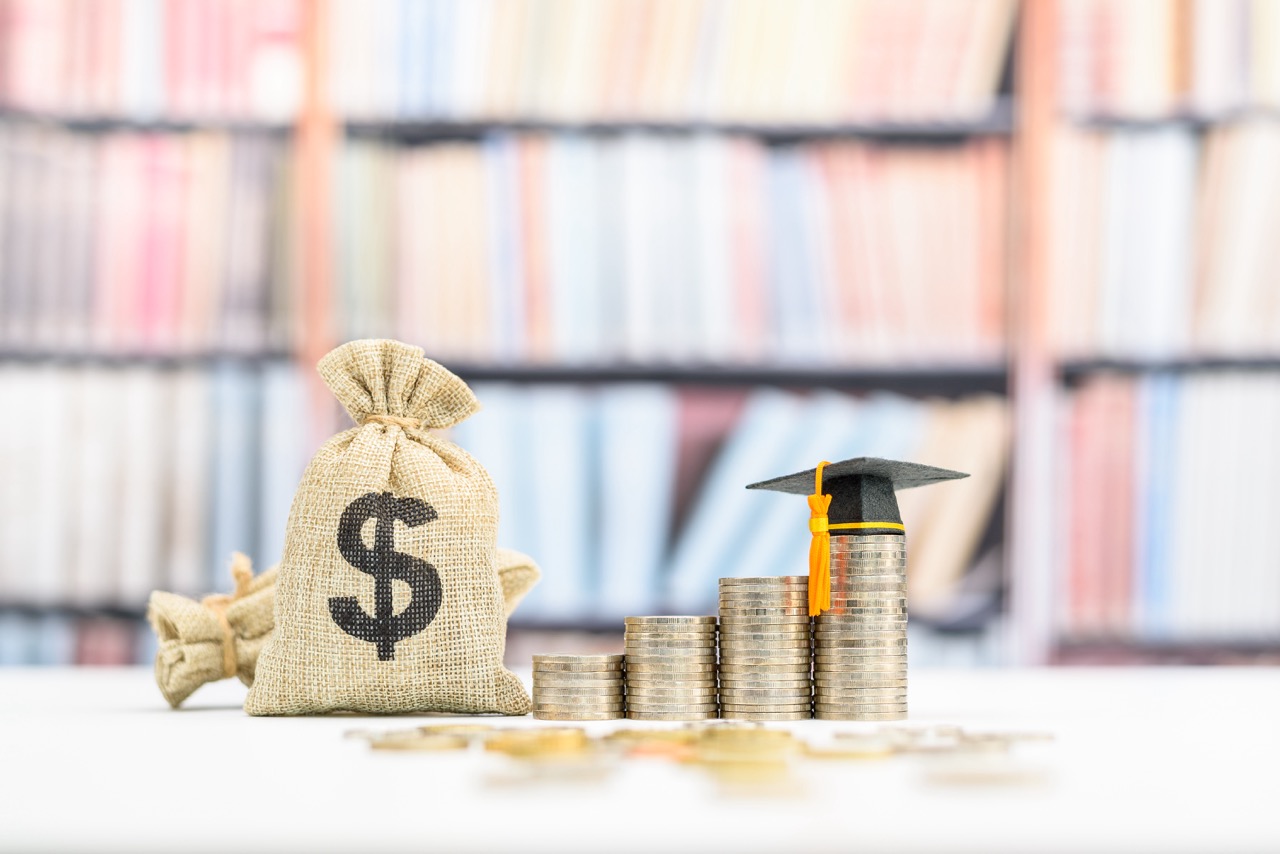Tuition payment or tuition fee, expense for graduate study abroad program concept : Black graduation cap on stacks of coins, depicting fees charged by education institution for instruction or services